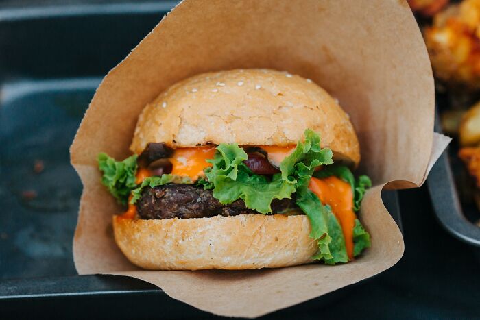 Close-up of a cheeseburger with lettuce and sauce wrapped in paper, illustrating customers’ ridiculous complaints for employees.