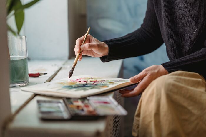 Person creating fan art with paintbrush and watercolors, focusing on detailed movie-inspired artwork.