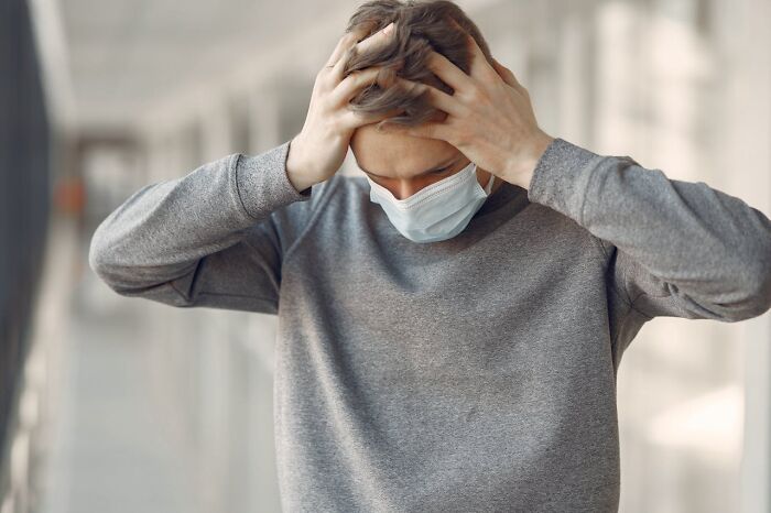Stressed medical staff wearing mask, holding head in hands after witnessing horrible things in the ER.