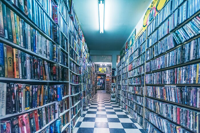 A narrow aisle in a video store filled with movie titles on shelves, perfect for movie trivia and cinephile challenges.