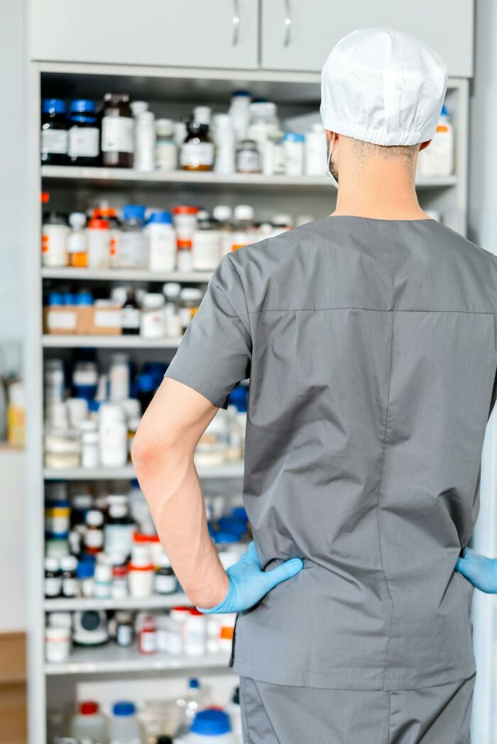 Pharmacist in gray scrubs and blue gloves standing in front of medicine shelves, illustrating things people said serious but sounded like jokes.