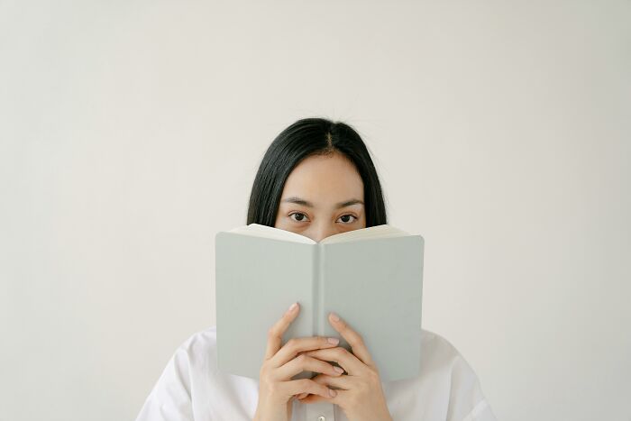 Young woman holding a book up to her face, focused on spelling and grammar check while reading quietly.