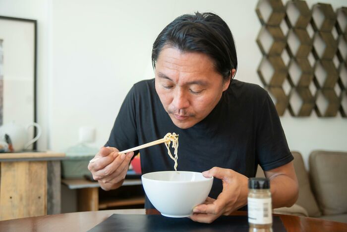 Man using chopsticks to eat noodles from a bowl, showing wholesome dads supporting their kids in everyday moments