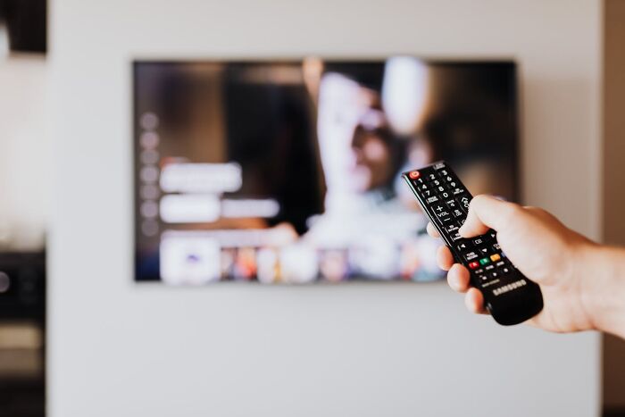 Person holding remote control pointing at TV screen showing a blurred video, illustrating disastrous first dates concept.