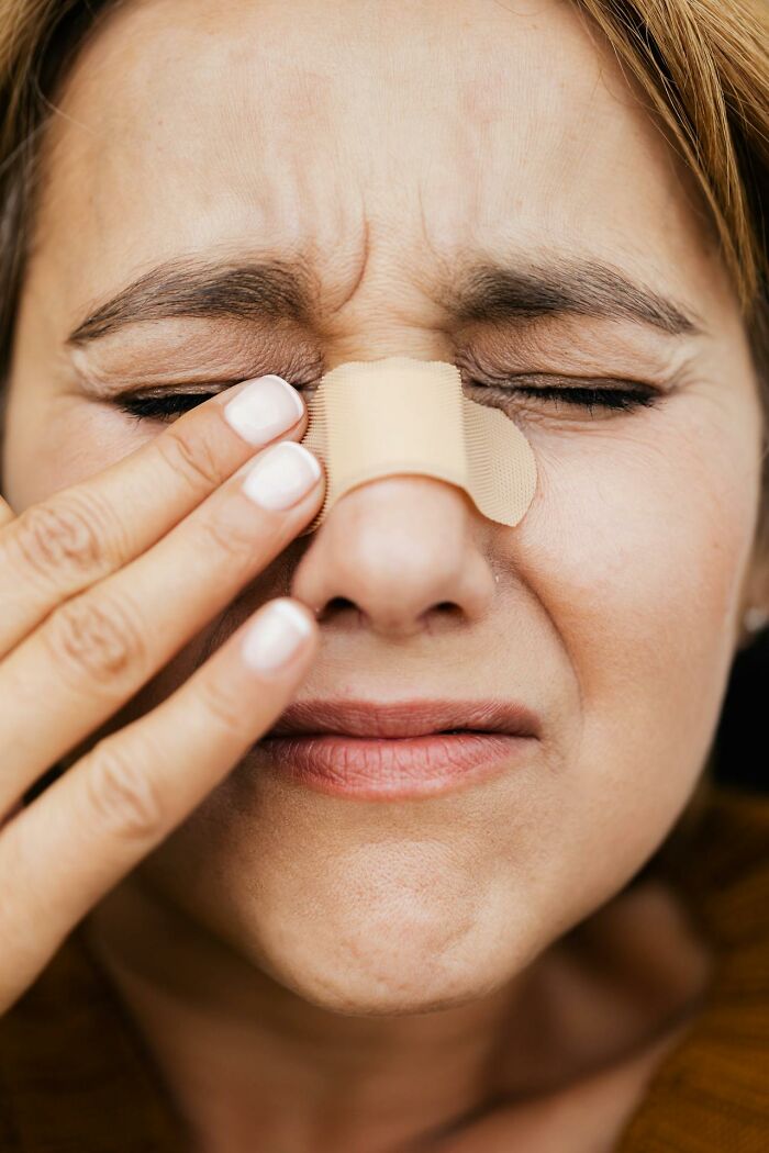 Close-up of woman with a painful expression holding a bandage on her nose after a disastrous first date experience.