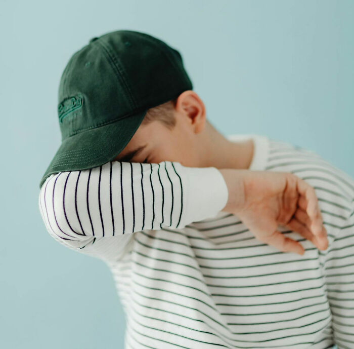 Young man in striped shirt and cap covering face with arm, illustrating disastrous first dates and dating challenges emotions.