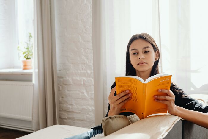 Young woman reading a book indoors, focused on guessing the word from 30 hints in a mind reading challenge.