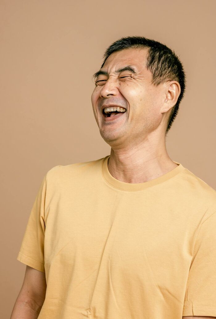 Man in yellow t-shirt laughing joyfully, capturing moments of things people said that sounded like a complete joke.
