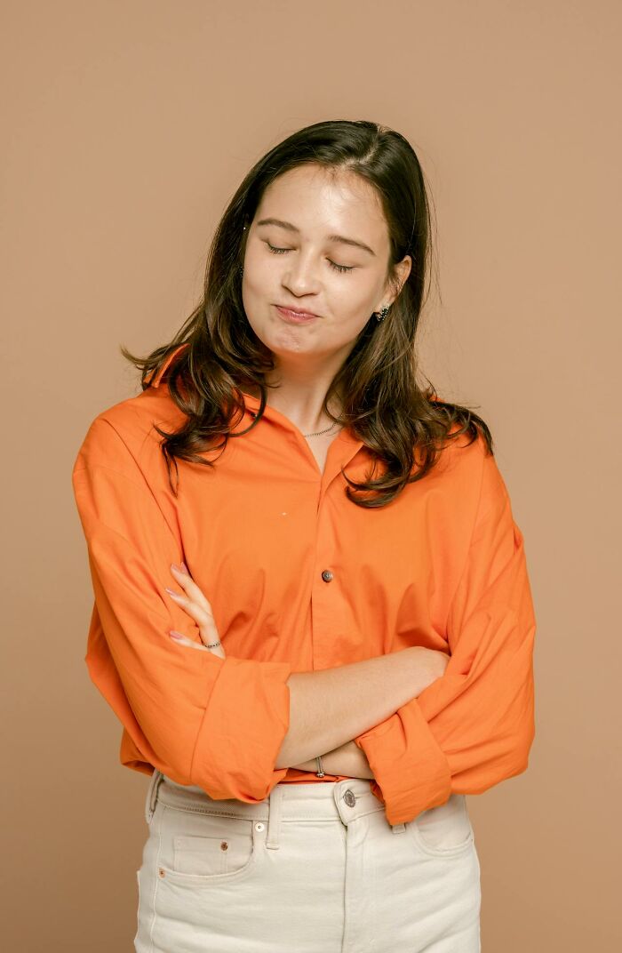 Young woman in an orange shirt with arms crossed, expressing a thoughtful and serious look for people said that sounded like joke.