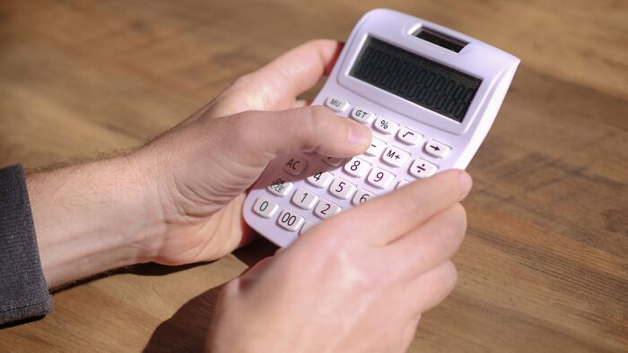 Hands holding a white calculator on a wooden table illustrating bizarre true stories involving unexpected numbers or facts.