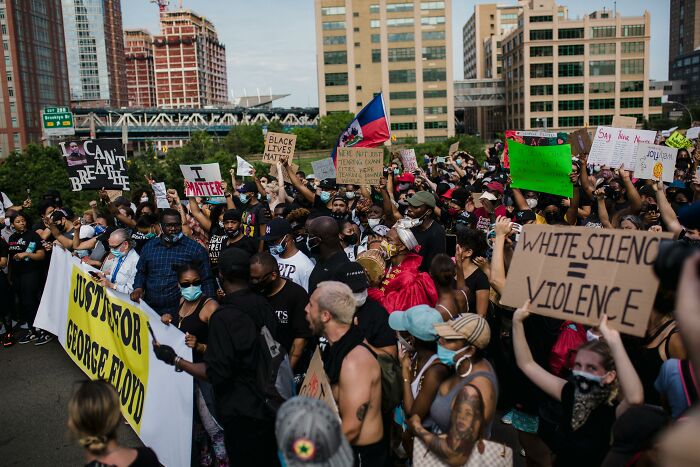 Crowd holding protest signs about racial justice and police brutality in an urban setting, reflecting vanished societal truths.