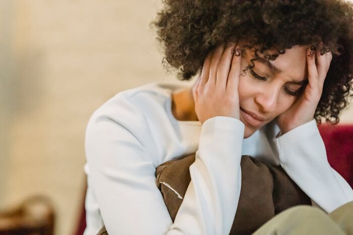 Woman with curly hair looking stressed and overwhelmed, holding her head while sitting indoors, life hacks regret concept.