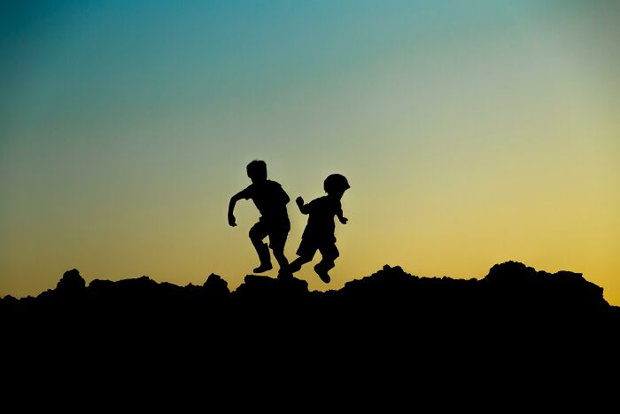 Silhouettes of two children jumping on rocky terrain at sunset, challenging you to recognize famous characters.