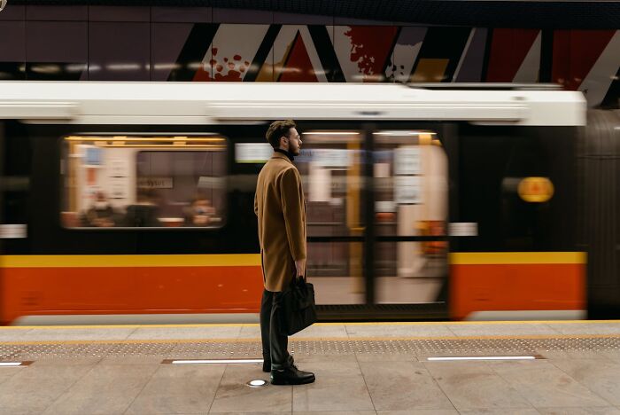 Man in a brown coat standing at a subway platform with a blurred train passing by, illustrating bizarre true stories.