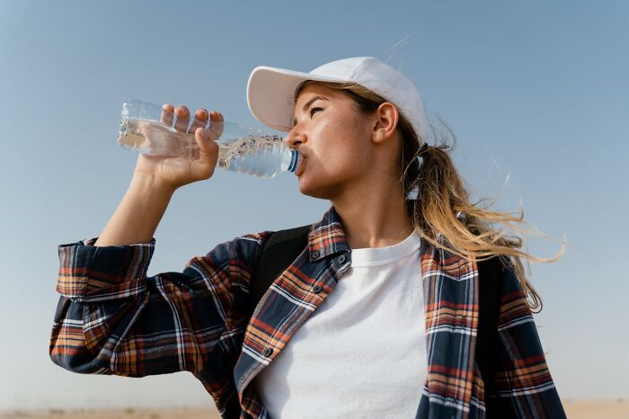 Young woman drinking water outdoors wearing a cap and plaid shirt, reflecting things people said that sounded like a joke but serious