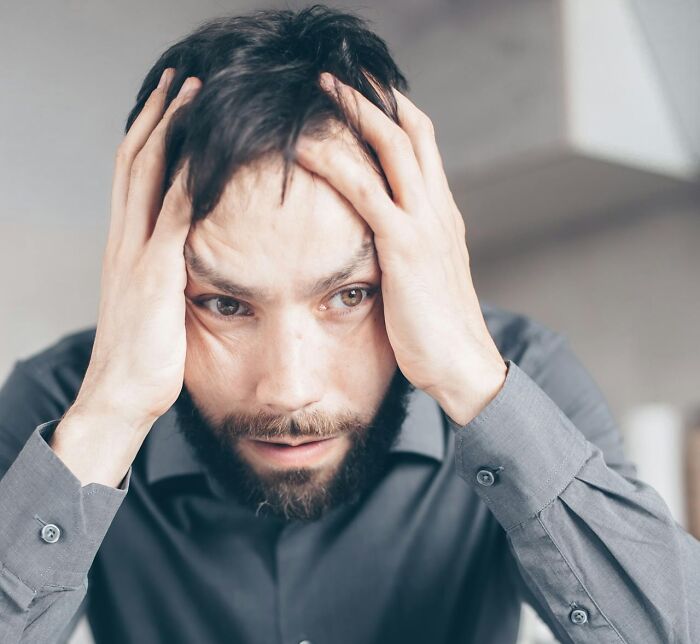 Stressed man with beard holding his head, representing the impact of women shutting down men’s creepy advances.