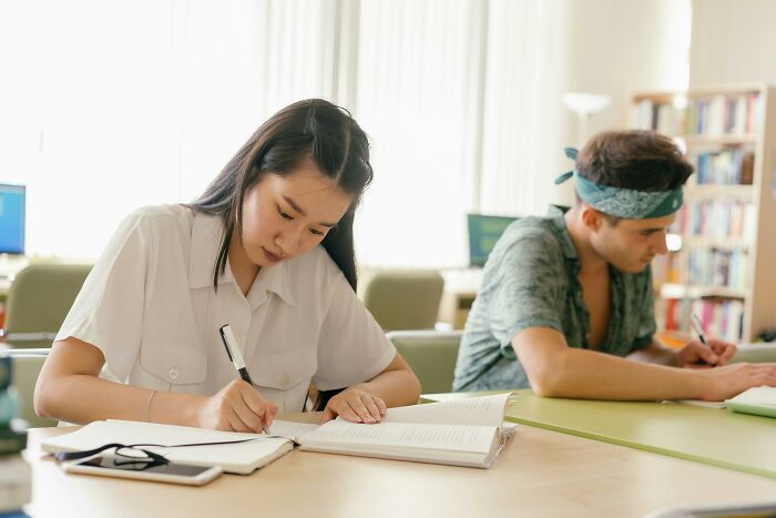 Two students focused on writing while studying advanced general knowledge questions in a bright classroom setting