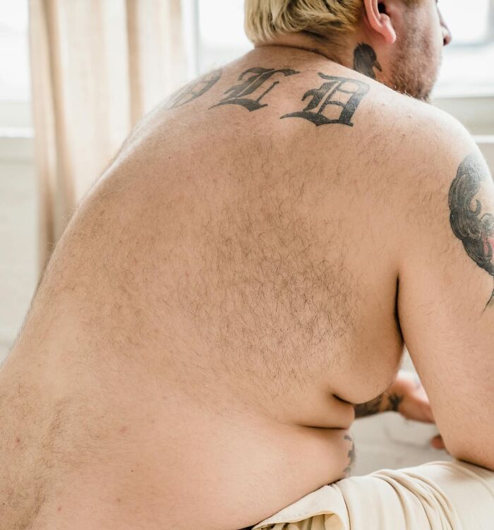 Man with tattoos on back and shoulder sitting shirtless near window, representing creepy advances in social contexts.