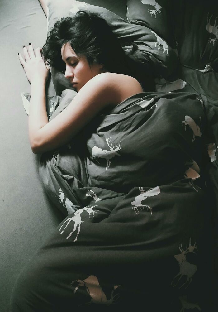 Woman sleeping alone in bed under dark moose-patterned blanket, reflecting on disastrous first dates and dating experiences.