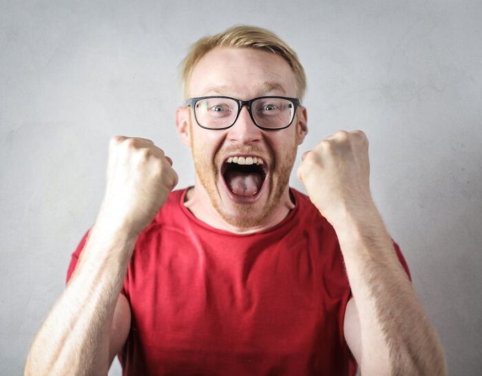 Man in red shirt with glasses excitedly raising fists, representing true stories that sound bizarre and unbelievable.