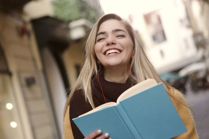 Young woman smiling and reading a book outdoors, enjoying bizarre true stories that sound unbelievable.