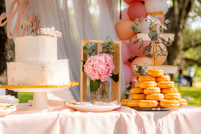 Wedding dessert table with cake, donuts, and floral decorations at an outdoor event with caterers present Wedding dessert table with cake, donuts, and floral decorations at an outdoor event with caterers present