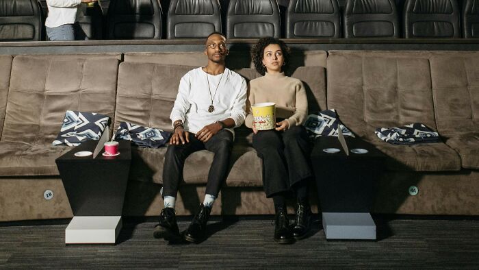 Two people sitting in a cinema holding popcorn and drinks, watching movies and TV shows, guessing visuals. Two people sitting in a cinema holding popcorn and drinks, watching movies and TV shows, guessing visuals.