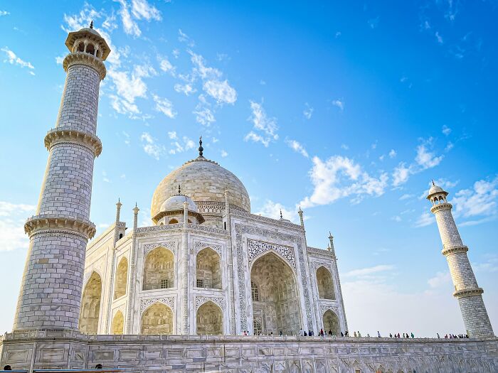 Taj Mahal under a bright blue sky, a famous iconic landmark surrounded by tourists on a clear day.