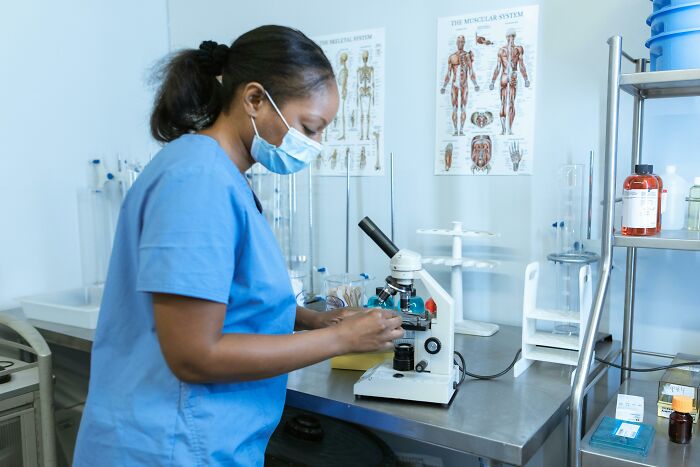 Medical lab technician wearing mask using microscope in clinical lab, symbolizing patient sample handling and doctor secrets.