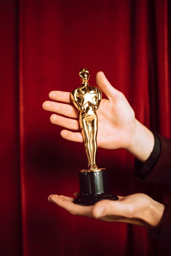 Hands holding a golden trophy statue against a red curtain background, illustrating surprising serious statements.