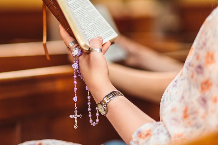Person holding a rosary and reading a book, symbolizing moments from disastrous first dates that challenge dating experiences.
