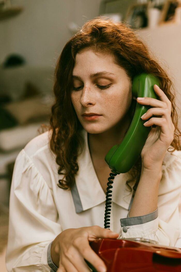 Young woman with red curly hair using a vintage green phone, capturing moments that sounded like a complete joke but were serious.