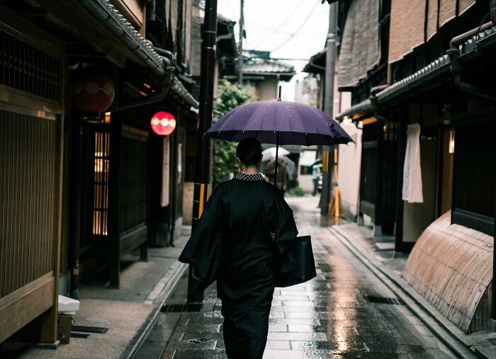 Person walking under an umbrella on a rainy street, illustrating truths that have sadly vanished from home countries.
