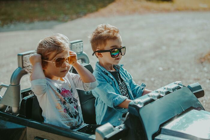 Two kids wearing sunglasses sitting in a toy car, representing tough reasons in a relationship despite hating partner.