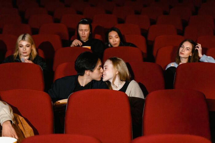 Couple on a disastrous first date kissing in a crowded theater while others show awkward or disinterested dating reactions.
