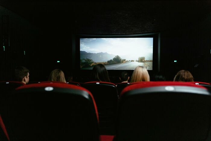Audience seated in a dark theater watching a scenic road on screen, illustrating customer complaints making employees laugh.