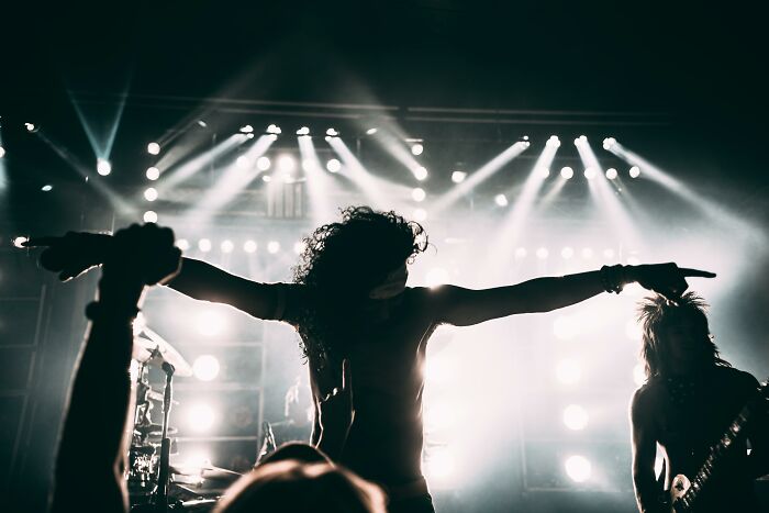 Silhouetted 80s rock band performing on stage with bright lights and enthusiastic crowd, capturing millennial music nostalgia.