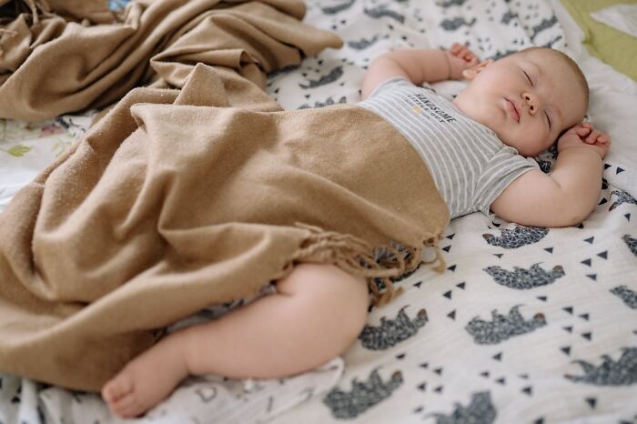 Sleeping baby wrapped in a brown blanket on patterned sheets, peaceful scene unrelated to medical staff or ER experiences.