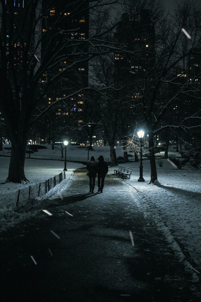 Couple walking on a snow-covered park path at night under streetlights, reflecting on disastrous first dates.