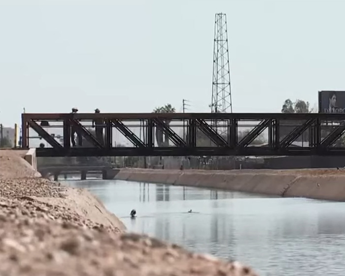 Metal bridge over a canal with people and an investigator in the water searching in Nancy Guthrie case FBI analysis.