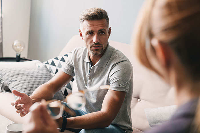 Man gesturing and mansplaining during a conversation with a woman in a casual living room setting.