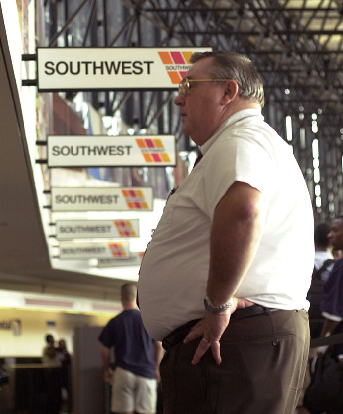 Homem esperando no terminal do aeroporto com placas da Southwest visíveis, relacionadas à reação da política de tamanho do cliente da companhia aérea.