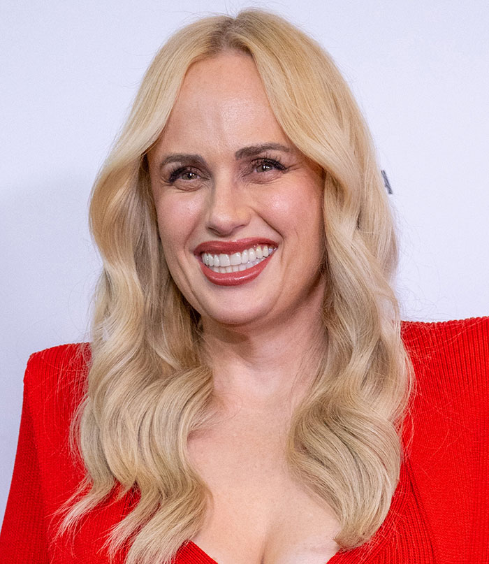 Blonde woman smiling with curled hair and red dress, illustrating tired eyes despite youthful faces and sleepiness.
