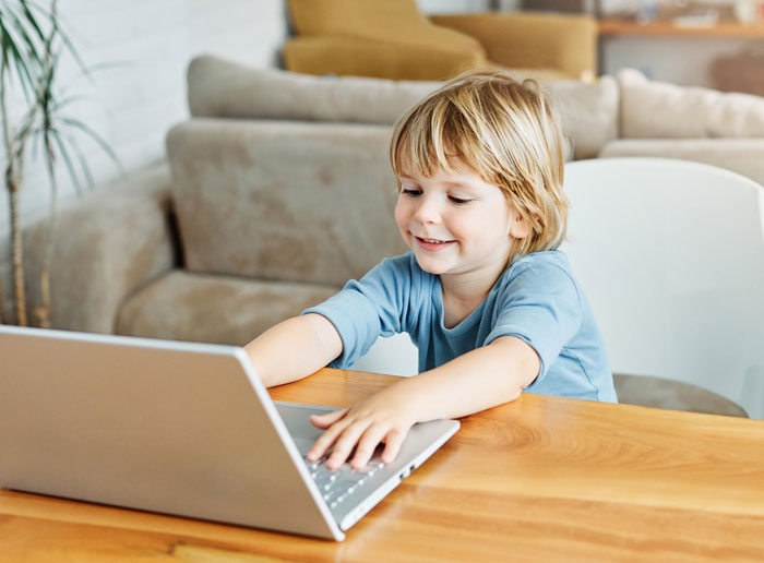 Young 3-year-old boy being a menace while using laptop, sister frustrated with his disruptive behavior at home.