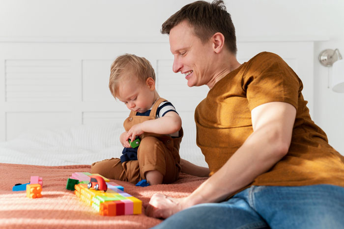 Man watches his 3-year-old son playing with toys while sister looks frustrated at the son's disruptive behavior.