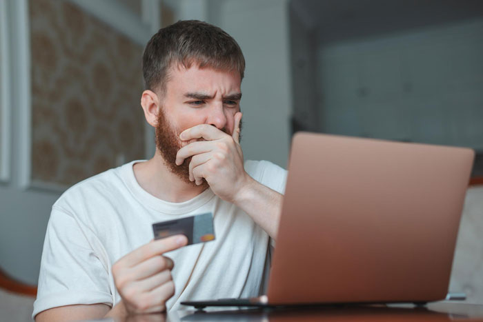 Man looking shocked while holding a credit card and viewing an expensive woman&rsquo;s dream ring price online.