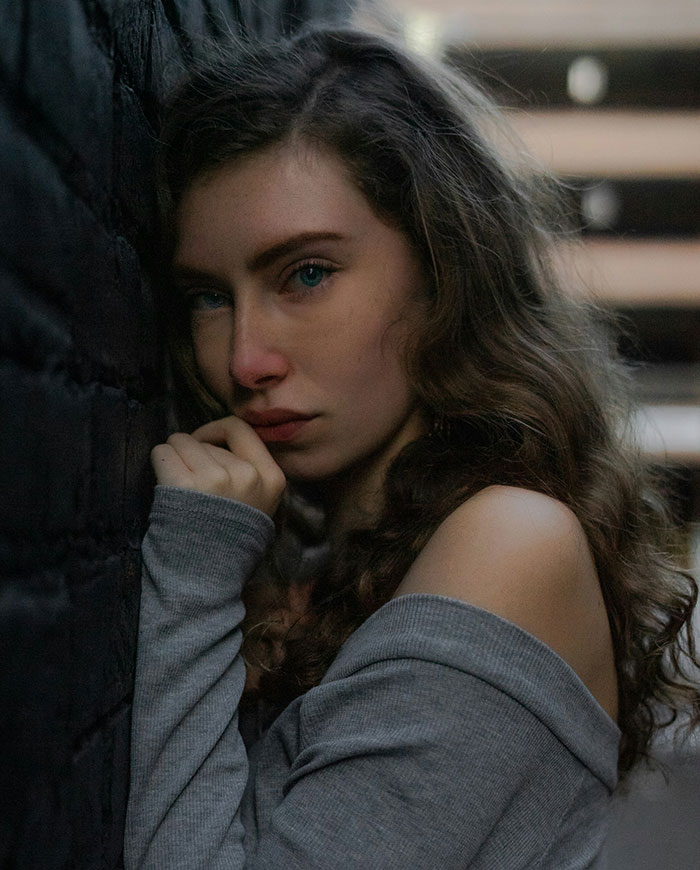 Young woman with curly hair leaning against a wall, looking sad and thoughtful in an intimate portrait on proposal embarrassment.