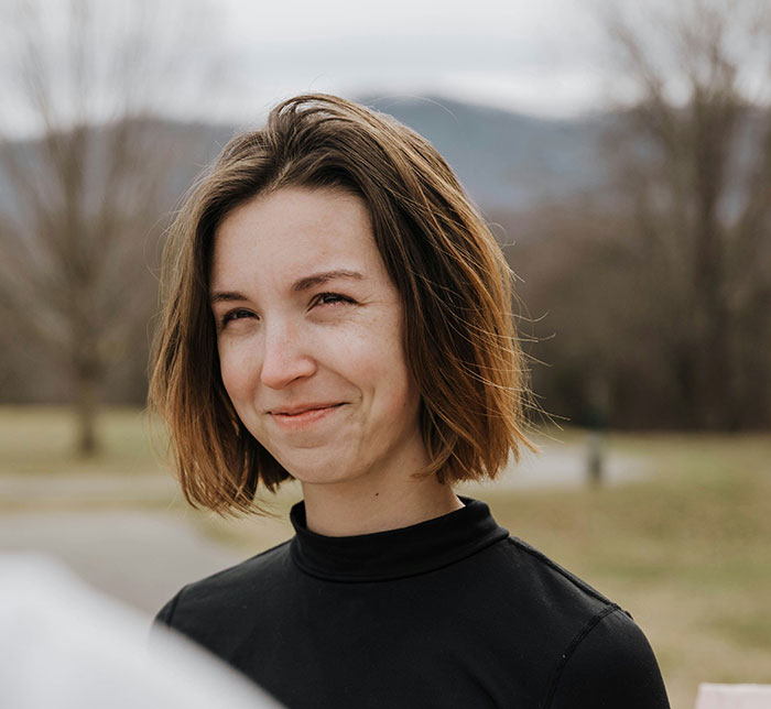Young woman outdoors with a subtle smile, reflecting on moments when people popped the question awkwardly.