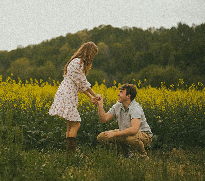 Man kneeling in a field proposing marriage to a woman, capturing the moment of popping the question outdoors.