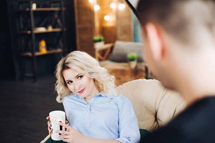 A woman sitting on a couch holding a mug, with a man nearby, capturing a candid moment of a popped the question scenario.